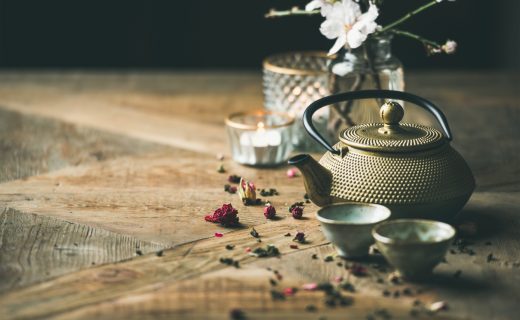 Traditional Asian tea ceremony arrangement. Golden iron teapot, lagares, candles y almond blossom flowers over vintage wooden table background, copy space, selective focus